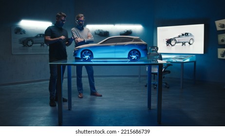 Senior Automotive Engineers Examine The Prototype Car Model Placed On A Glass Table In Different Shades And Colors Of Light. Using A Digital Touchscreen Tablet In A Hightech Car Manufacturing Company.