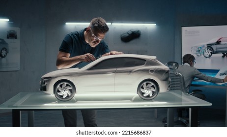 Senior Automotive Engineers Work In High Tech Car Manufacturing Company. One Of Them Works On The Sculpture Of The Prototype Car While The Other One Uses A Digital Touch Screen Table To Draw Sketches.