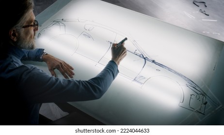 Senior automotive male designer drawing sketch blueprint with marker at the light table, developing futuristic electric car future design. He working in modern car design development studio. - Powered by Shutterstock