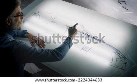 Senior automotive male designer drawing sketch blueprint with marker at the light table, developing futuristic electric car future design. He working in modern car design development studio.