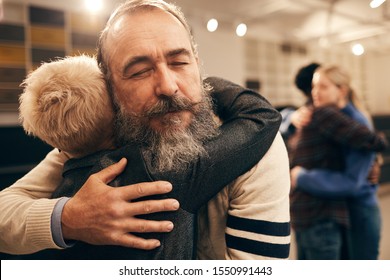 Senior bearded man embracing woman and enjoying the hug during therapy with other couple in the background - Powered by Shutterstock