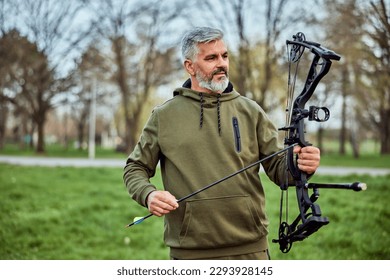 A senior bearded man looking focused while holding a bow and arrow in archery. - Powered by Shutterstock