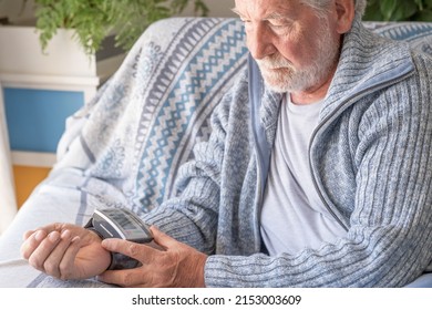 Senior bearded man using medical device to measure blood pressure, elder grandfather sitting at home on sofa - Shutterstock ID 2153003609