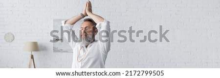 senior bearded man in white shirt meditating with arms up and praying hands, banner