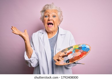 Senior beautiful grey-haired artist woman painting using brush and palette over pink background very happy and excited, winner expression celebrating victory screaming with big smile and raised hands - Powered by Shutterstock