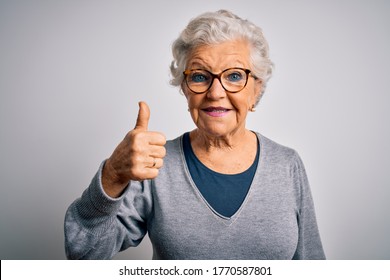Senior beautiful grey-haired woman wearing casual sweater and glasses over white background doing happy thumbs up gesture with hand. Approving expression looking at the camera showing success.