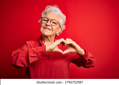 Senior beautiful grey-haired woman wearing casual shirt and glasses over red background smiling in love doing heart symbol shape with hands. Romantic concept. - Powered by Shutterstock