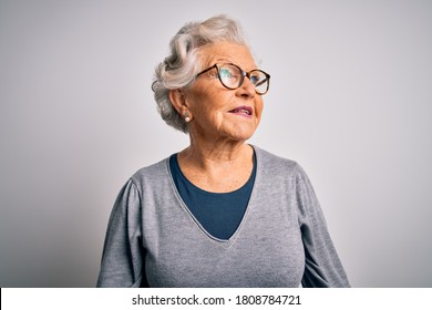 Senior beautiful grey-haired woman wearing casual sweater and glasses over white background looking away to side with smile on face, natural expression. Laughing confident.