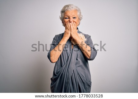 Senior beautiful grey-haired woman wearing casual dress standing over white background laughing and embarrassed giggle covering mouth with hands, gossip and scandal concept