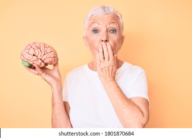 Senior beautiful woman with blue eyes and grey hair holding brain as mental health concept covering mouth with hand, shocked and afraid for mistake. surprised expression  - Shutterstock ID 1801870684