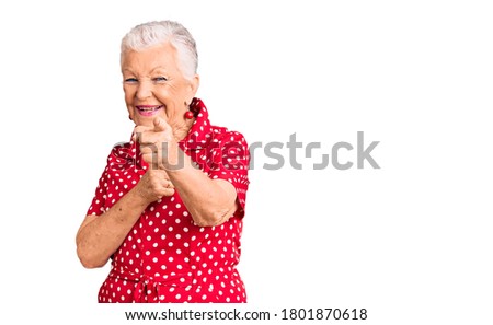 Senior beautiful woman with blue eyes and grey hair wearing a red summer dress pointing fingers to camera with happy and funny face. good energy and vibes. 