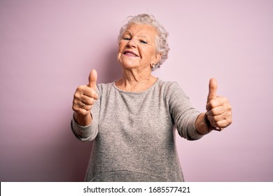 Senior beautiful woman wearing casual t-shirt standing over isolated pink background approving doing positive gesture with hand, thumbs up smiling and happy for success. Winner gesture.
