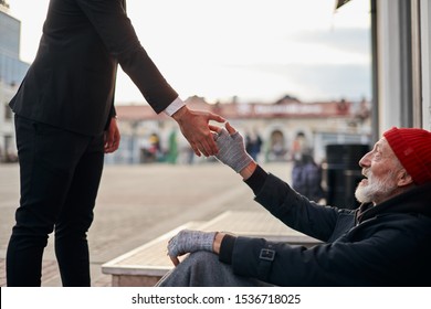 Senior beggar sitting beside street with request help with receive some coins from kind business man. Man hold out hand to homeless. - Powered by Shutterstock