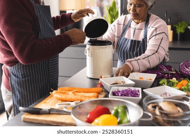 Senior biracial couple wearing aprons composting food waste in kitchen at home. Senior lifestyle, retirement, ecology, food, cooking and domestic life, unaltered. - Powered by Shutterstock