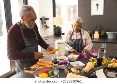 Senior biracial couple wearing aprons preparing vegetables and using tablet in kitchen at home. Senior lifestyle, retirement, communication, food, cooking and domestic life, unaltered. - Powered by Shutterstock