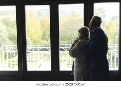 Senior biracial couple wearing bathrobes and drinking coffee by window at home, copy space. Senior lifestyle, retirement and domestic life, unaltered. - Powered by Shutterstock