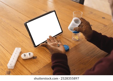 Senior biracial man having video call with doctor on tablet with copy space, holding pills at home. Senior lifestyle, retirement, communication, telemedicine and domestic life, unaltered. - Powered by Shutterstock