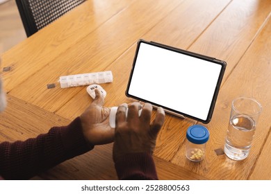 Senior biracial man having video call with doctor on tablet with copy space, holding pills at home. Senior lifestyle, retirement, communication, telemedicine and domestic life, unaltered. - Powered by Shutterstock