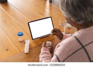 Senior biracial woman having video call with doctor on tablet with copy space, holding pills at home. Senior lifestyle, retirement, communication, telemedicine and domestic life, unaltered. - Powered by Shutterstock