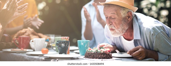 Senior birthday in. backyard tropical garden. White, asian senior man and woman with young couple. Enjoying a birthday party at home garden. Blowing candle. Banner frame and light leaks. - Powered by Shutterstock