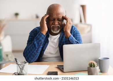 Senior Black Businessman Having Headache Touching Temples Suffering From Pain Using Laptop Computer Sitting At Desk In Modern Office. Health Problems, Migraine Symptom. Front View