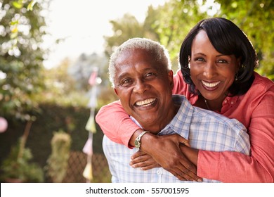 Senior Black Couple Piggyback In Garden Looking At Camera