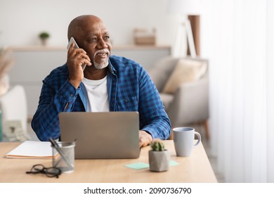 Senior Black Man At Laptop Talking On Phone Looking Aside Communicating For Work Sitting At Table In Office. Entrepreneur Chatting By Cellphone At Workplace. Mobile Communication - Powered by Shutterstock