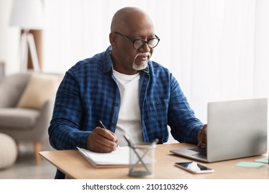 Senior Black Man Using Laptop And Writing Report Taking Notes Working Online Sitting At Desk In Office, Wearing Eyeglasses. Entrepreneurship In Mature Age, Business Lifestyle Concept