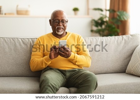 Senior Black Man Using Smartphone Texting Networking Online And Scrolling News In Social Media Application Sitting On Couch At Home. Mature Male Reading Message On Phone. New Mobile App Concept Stock foto © 