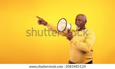 Senior black man yelling into megaphone, announcing news or message, pointing at blank space on orange background, banner design. Elderly African American male screaming with loudspeaker
