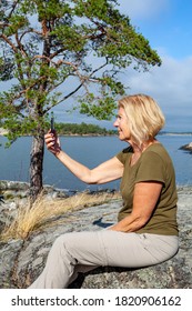 Senior Blonde Woman Calling Her Loved Ones On Facetime While Being Out Hiking On A Warm Summer Day In The Swedish Archipelago