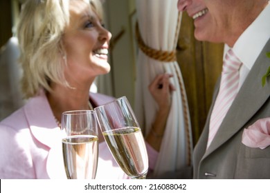 Senior bride and groom smiling at each other, toasting with champagne flutes, focus on glasses - Powered by Shutterstock