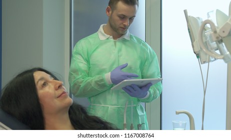Senior brunette woman demonstrating her teeth at the dentist. Mature female patient smiling for the camera on the dental chair. Camera pedding down from young dentist on background to his female - Shutterstock ID 1167008764