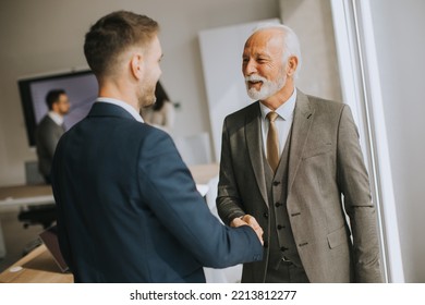 Senior business man handshaking with his young colleague in the office - Shutterstock ID 2213812277