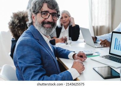 Senior Business Man Smiling At Camera While Working With Colleagues Inside Bank Office - Focus On Face