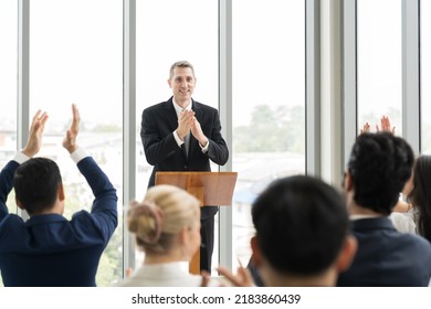 Senior Business Man Talking And Clapping Hands At Podium Speaker. Back View Of Business People Clapping Hands To Speaker At Business Conference Room