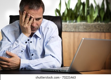 Senior Business Person In Blue Shirt Sitting At Office Desk Looking At Laptop And Being Frustrated About Computer Or Software Crash.