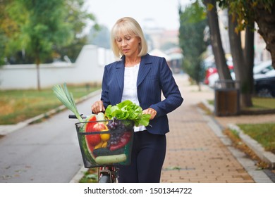 Senior Business Woman With Bike In A Street, Checking The Groceries In A Bicycle Basket.  Lifestyle Concept.