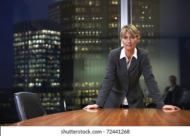 Senior Business Woman Leaning On Table In Boardroom Looking At Camera