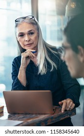 Senior Business Woman Listening To Her Male Colleague During Meeting In Office. Mature Female Paying Attention To The Discussing In Meeting.