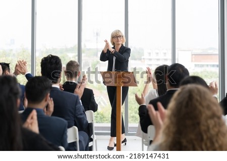 Senior business woman talking at podium speaker. Business people clapping hands to speaker at Business Conference