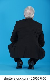 Senior Businessman Crouching With His Back To The Camera