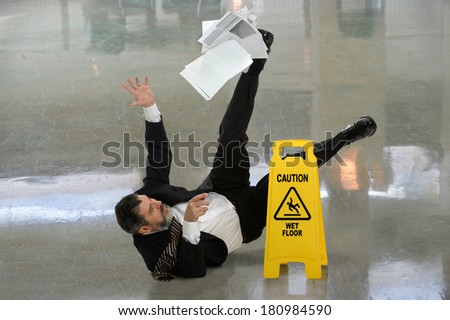 Senior businessman falling on wet floor in front of caution sign