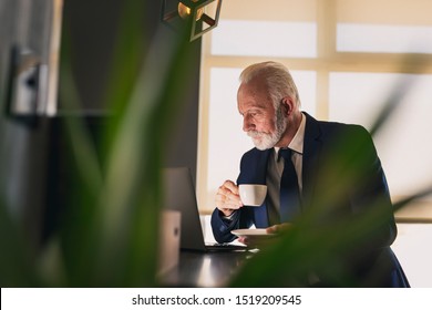 Senior businessman in a modern office working on a laptop computer and drinking coffee - Powered by Shutterstock