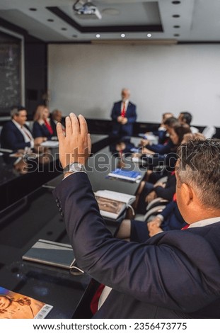 Senior businessman raising hand to ask question during meeting at the office.
