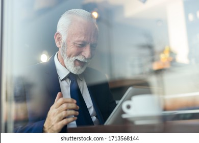 Senior Businessman In A Restaurant, Using A Tablet Computer And Drinking Coffee