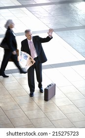 Senior Businessman Standing In Airport, Holding Financial Newspaper, Waving, Elevated View