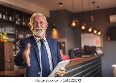 Senior Businessman Standing Next To A Modern Office Building Restaurant Counter, Waiting For A Meeting And Offering Hand For Handshake To Colleague