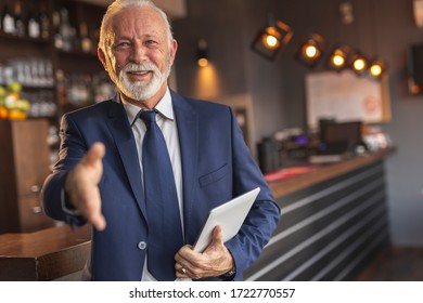 Senior Businessman Standing Next To A Modern Office Building Restaurant Counter, Waiting For A Meeting And Offering Hand For Handshake To Colleague