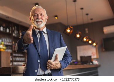 Senior Businessman Standing Next To A Modern Office Building Restaurant Counter, Waiting For A Meeting And Offering Hand For Handshake To Colleague